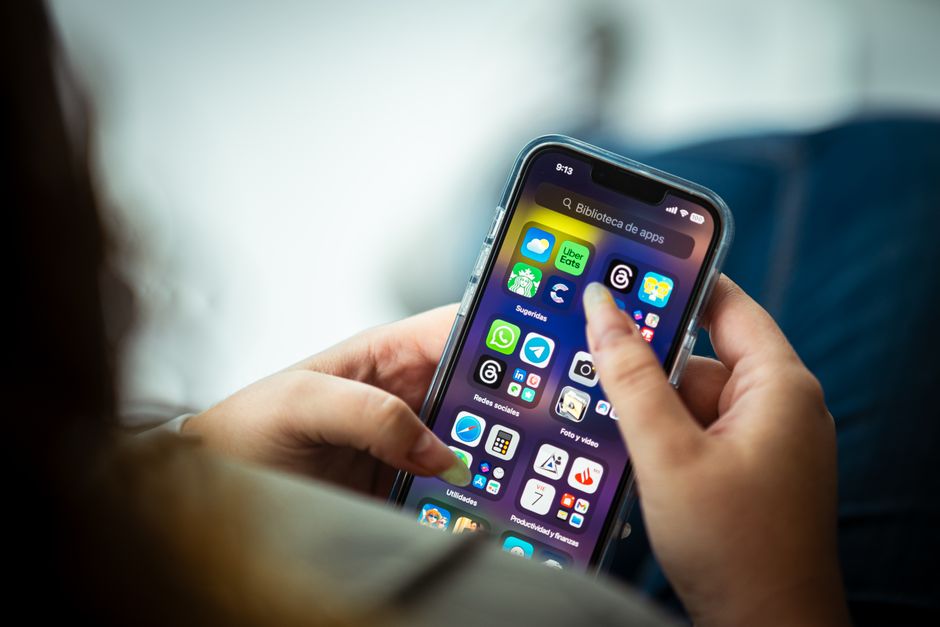 A person holds a smartphone and browses a list of apartments on Booking, with a finger ready to click on a featured listing.